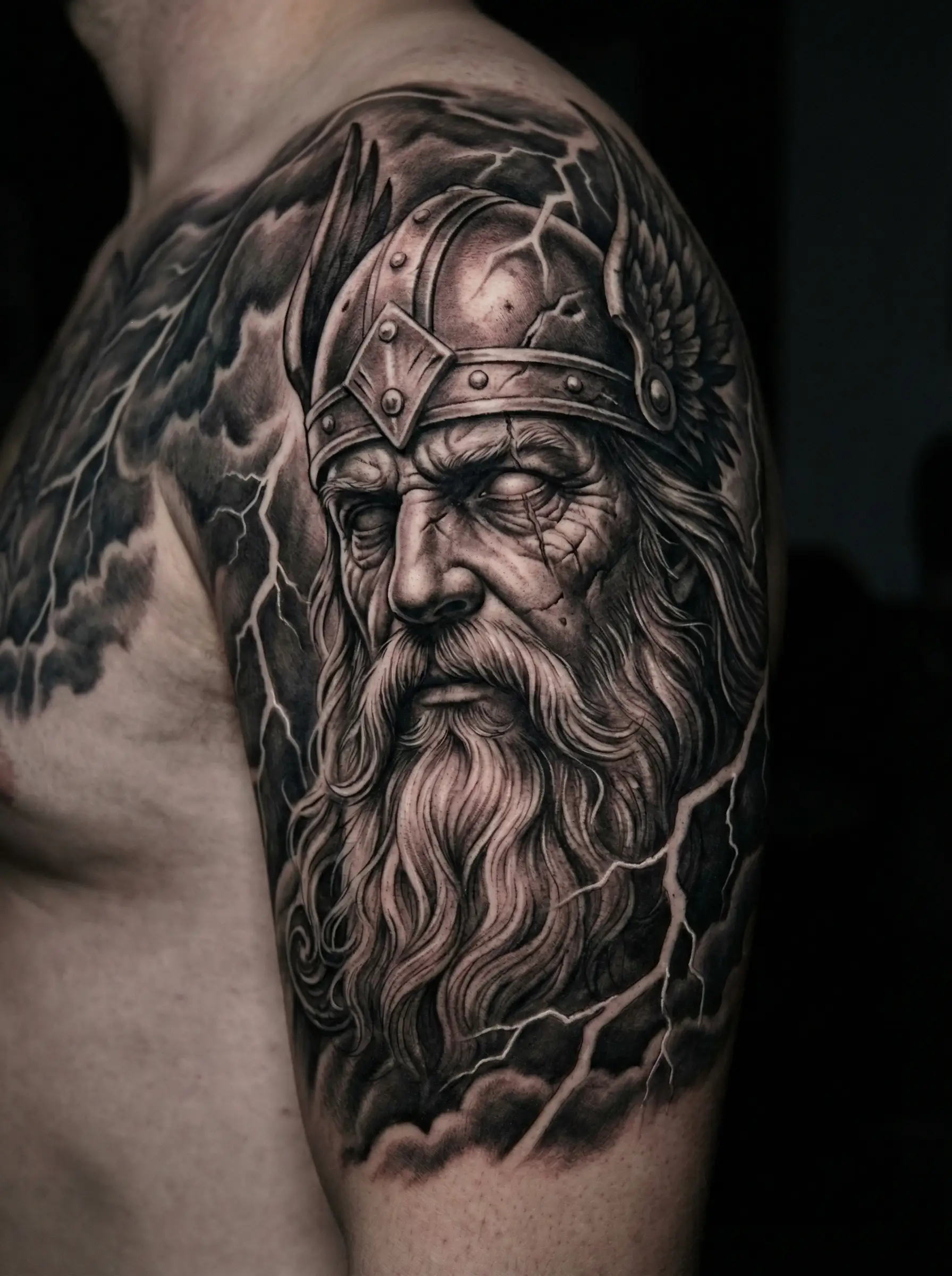 Реалистичная тату скандинавский бог Один в шлеме с крыльями на плече — black and grey реализм с молниями, тату ВДНХ